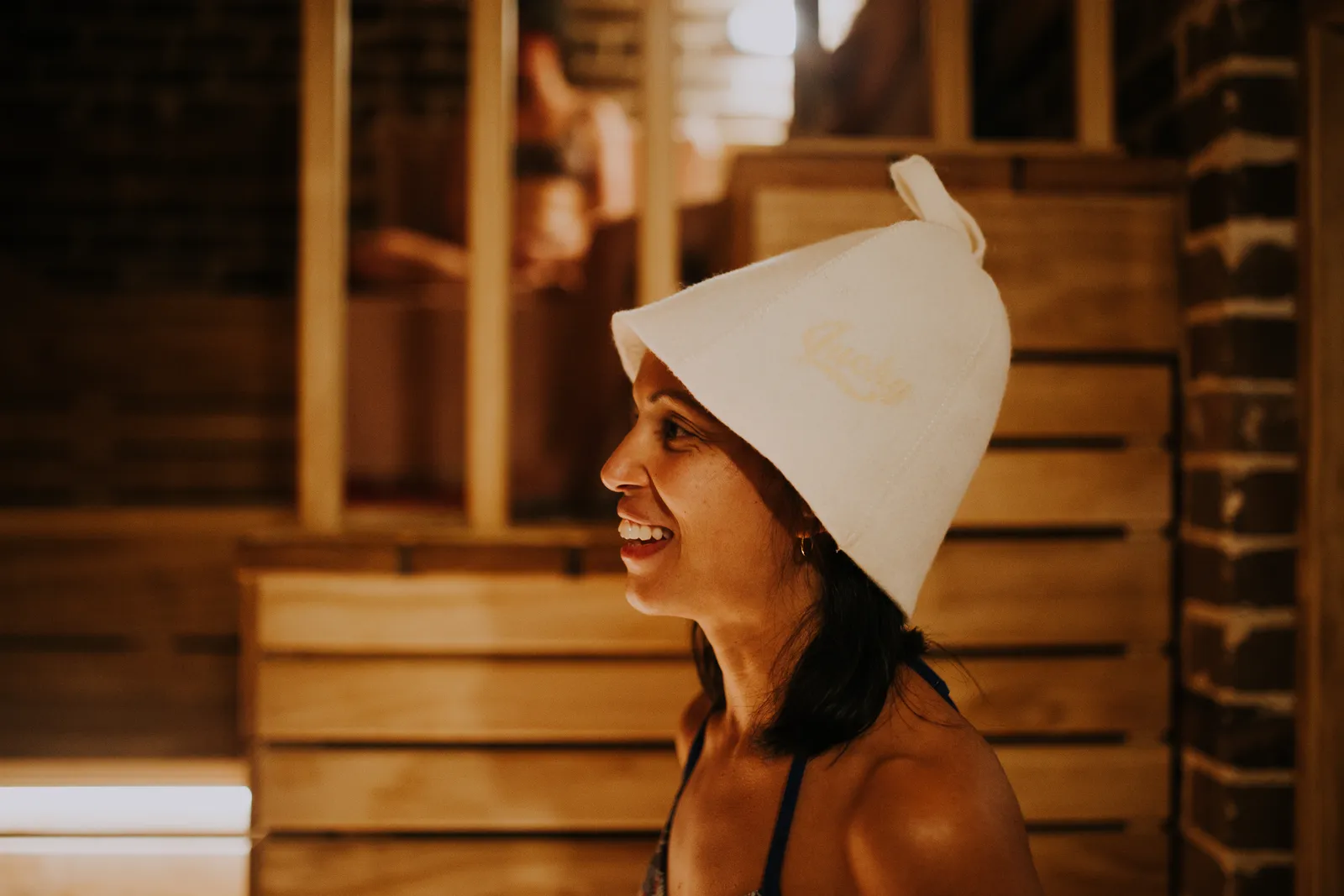 A first-time guest mid-laugh wearing a traditional Finnish felt sauna hat