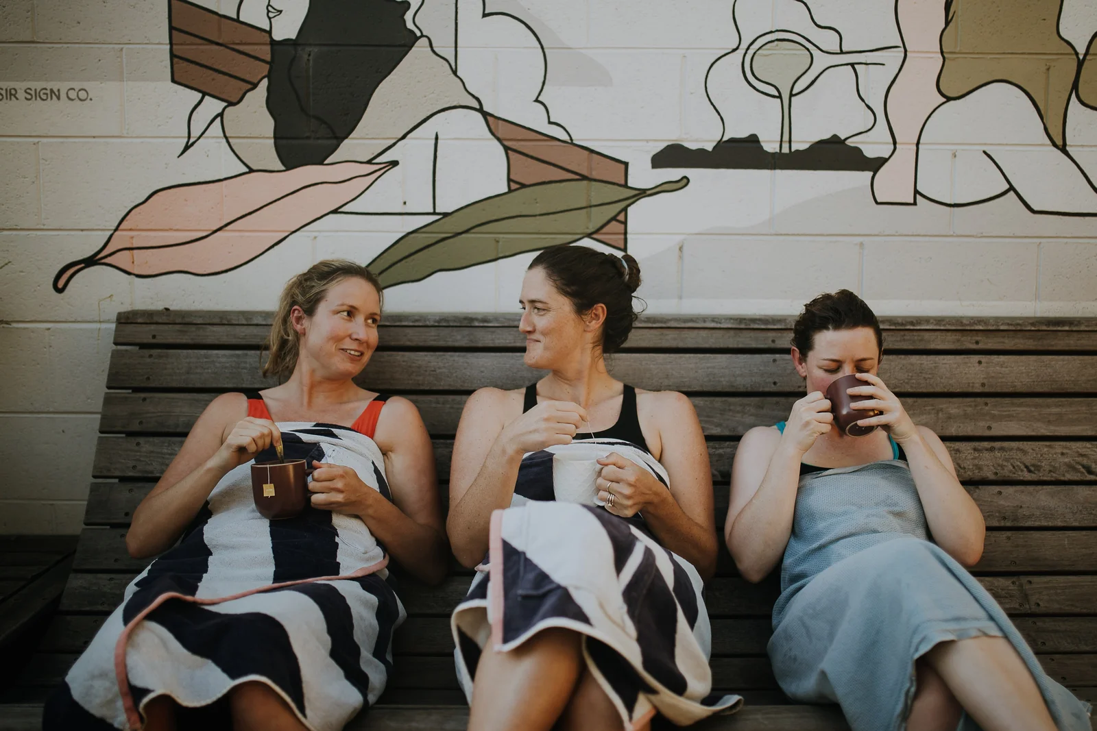 Three guests sharing tea on the courtyard bench under the mural