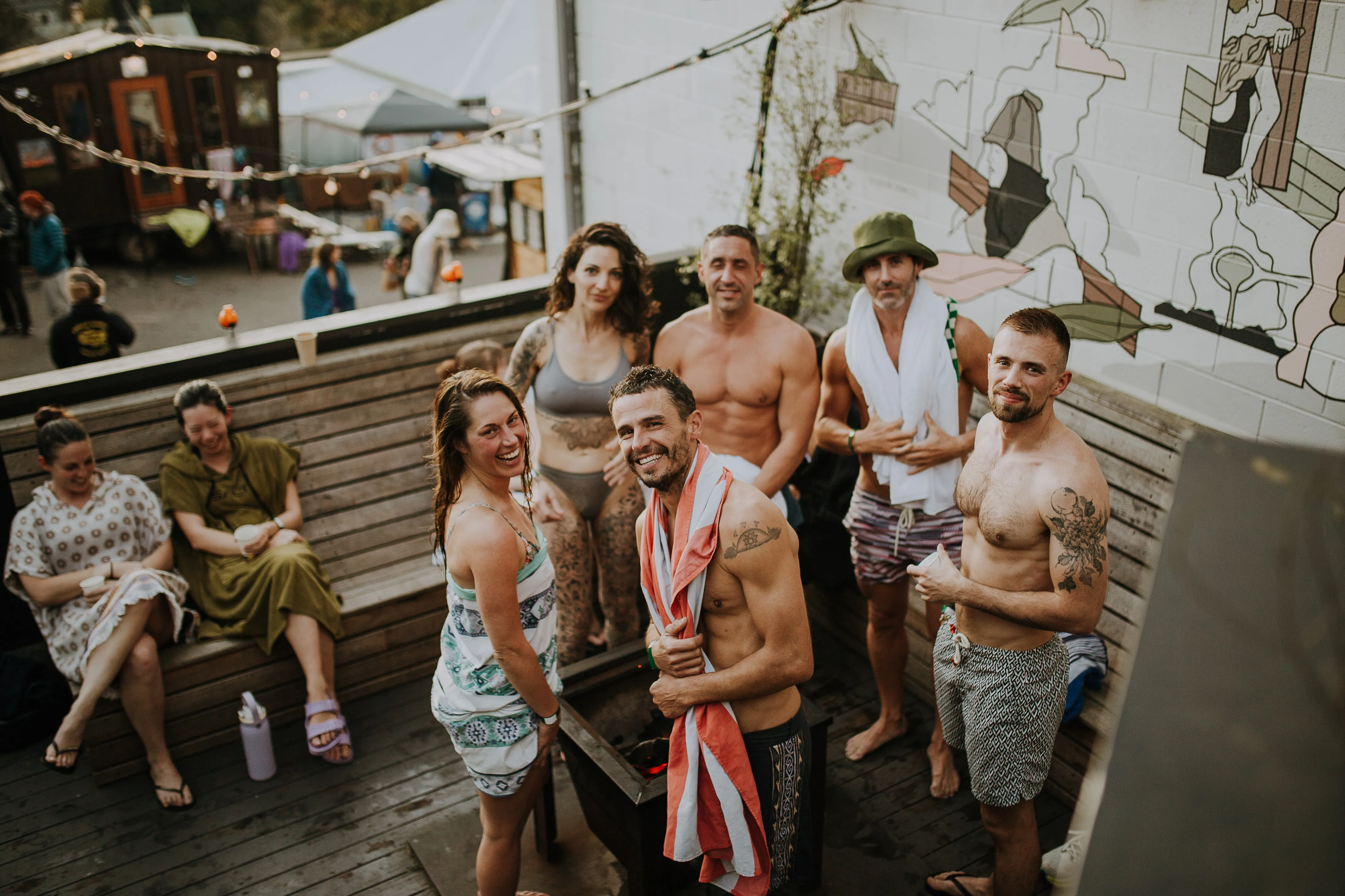 A group of smiling bathers gathered around the firepit on the deck at Blue Mountains Sauna