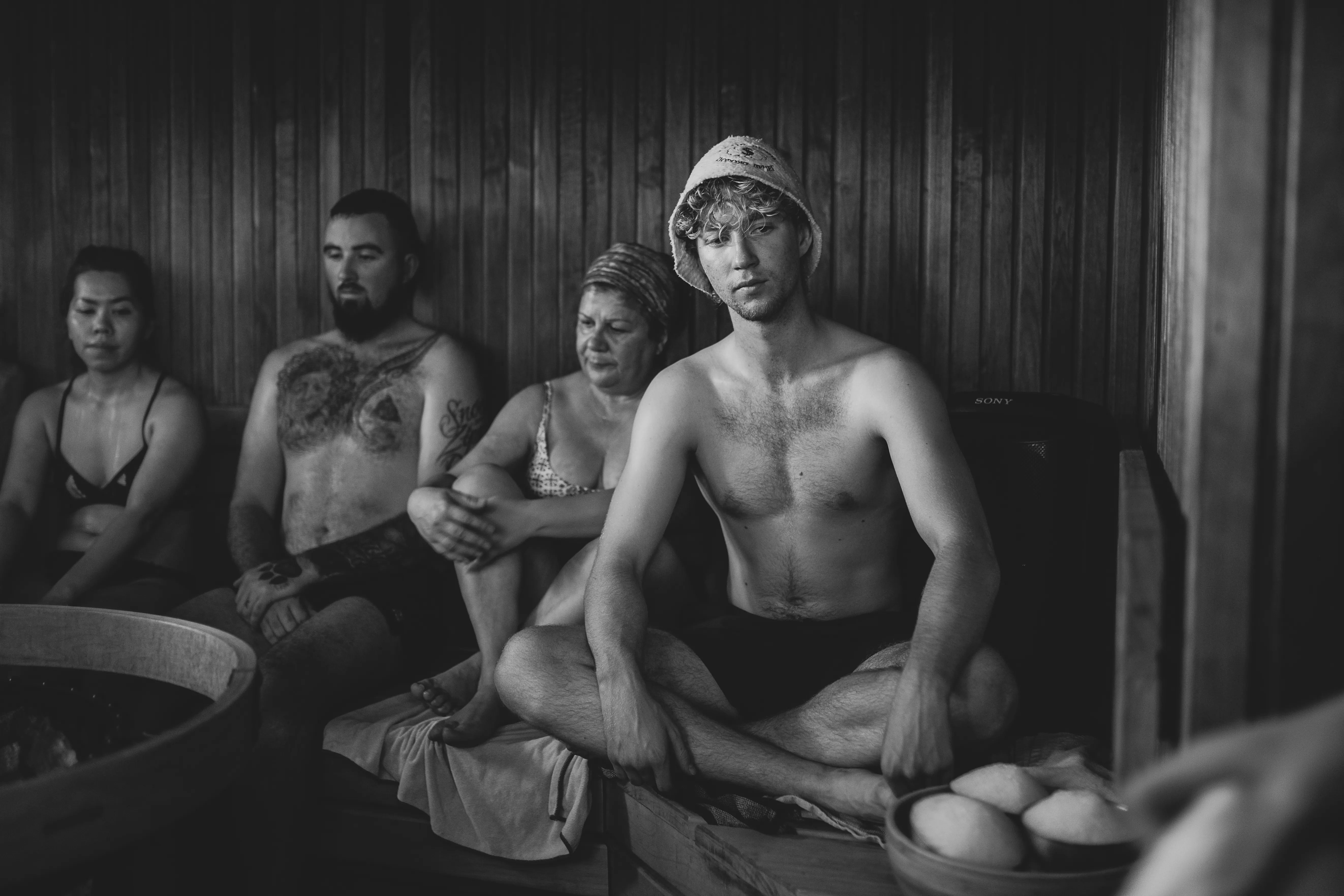 Bathers sitting together in the sauna, one wearing a felt sauna hat.