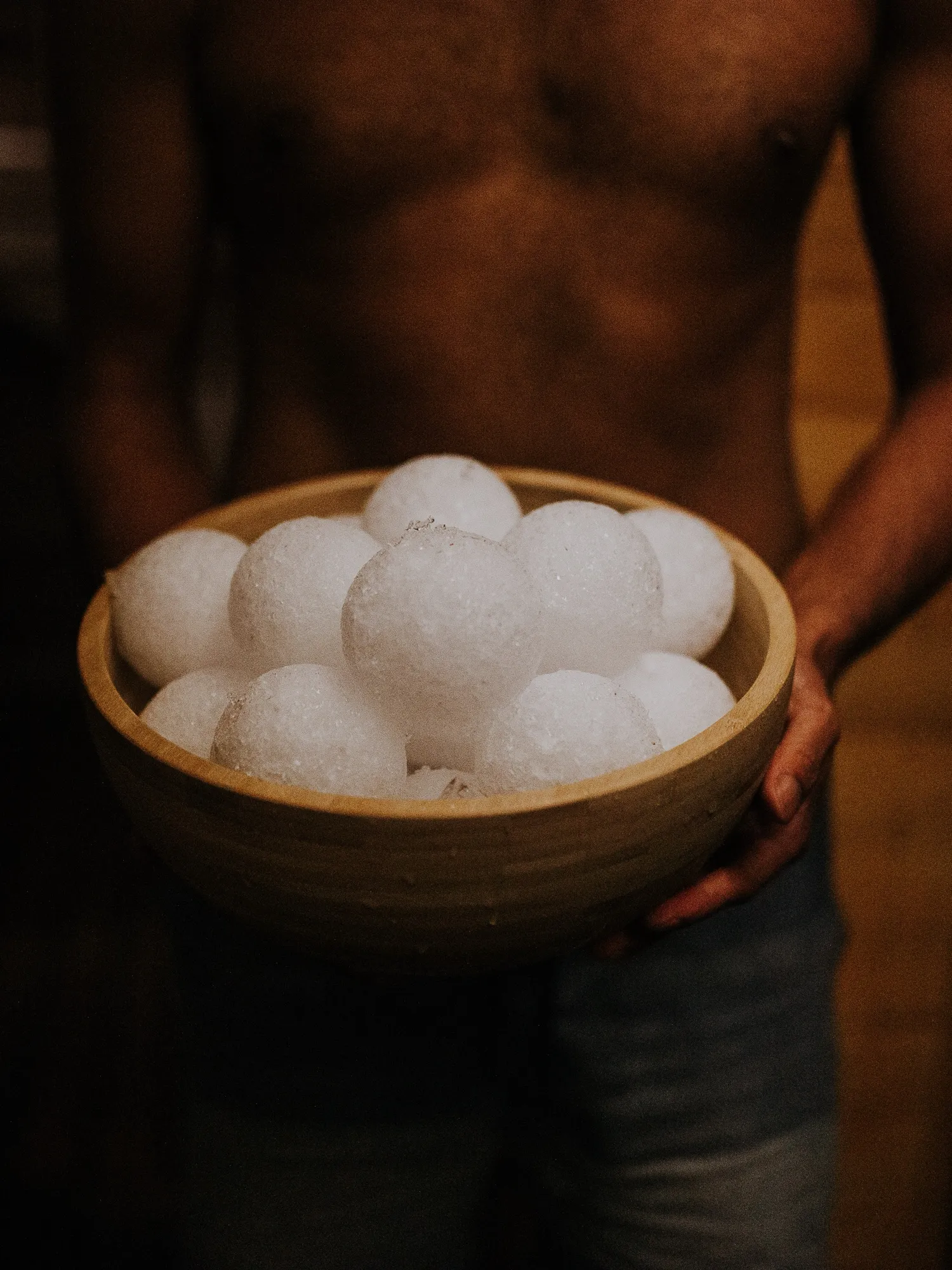 A bather holds a wooden bowl of ice balls