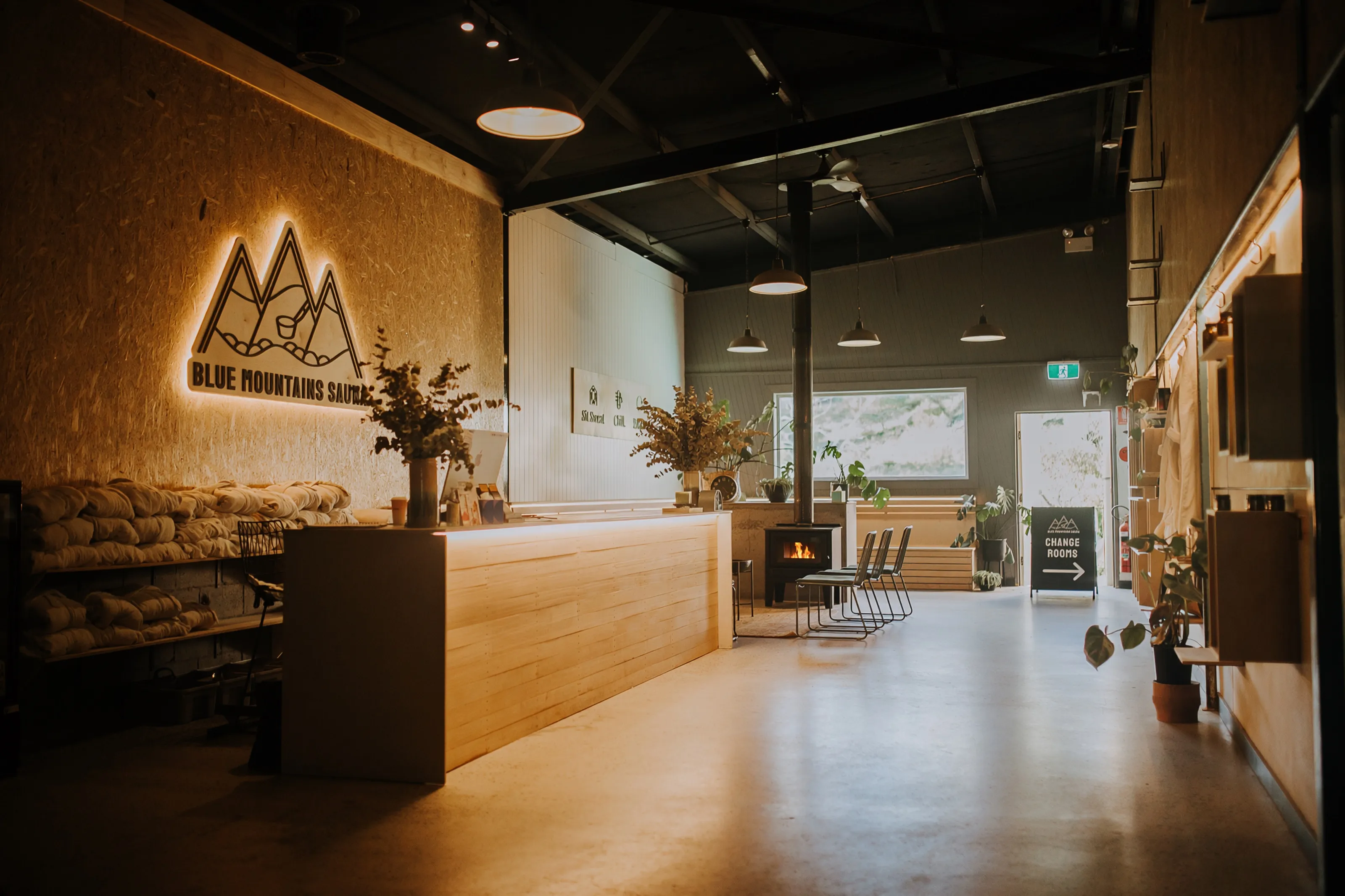 The Blue Mountains Sauna reception, with the logo lit on the timber wall and the open foyer beyond.