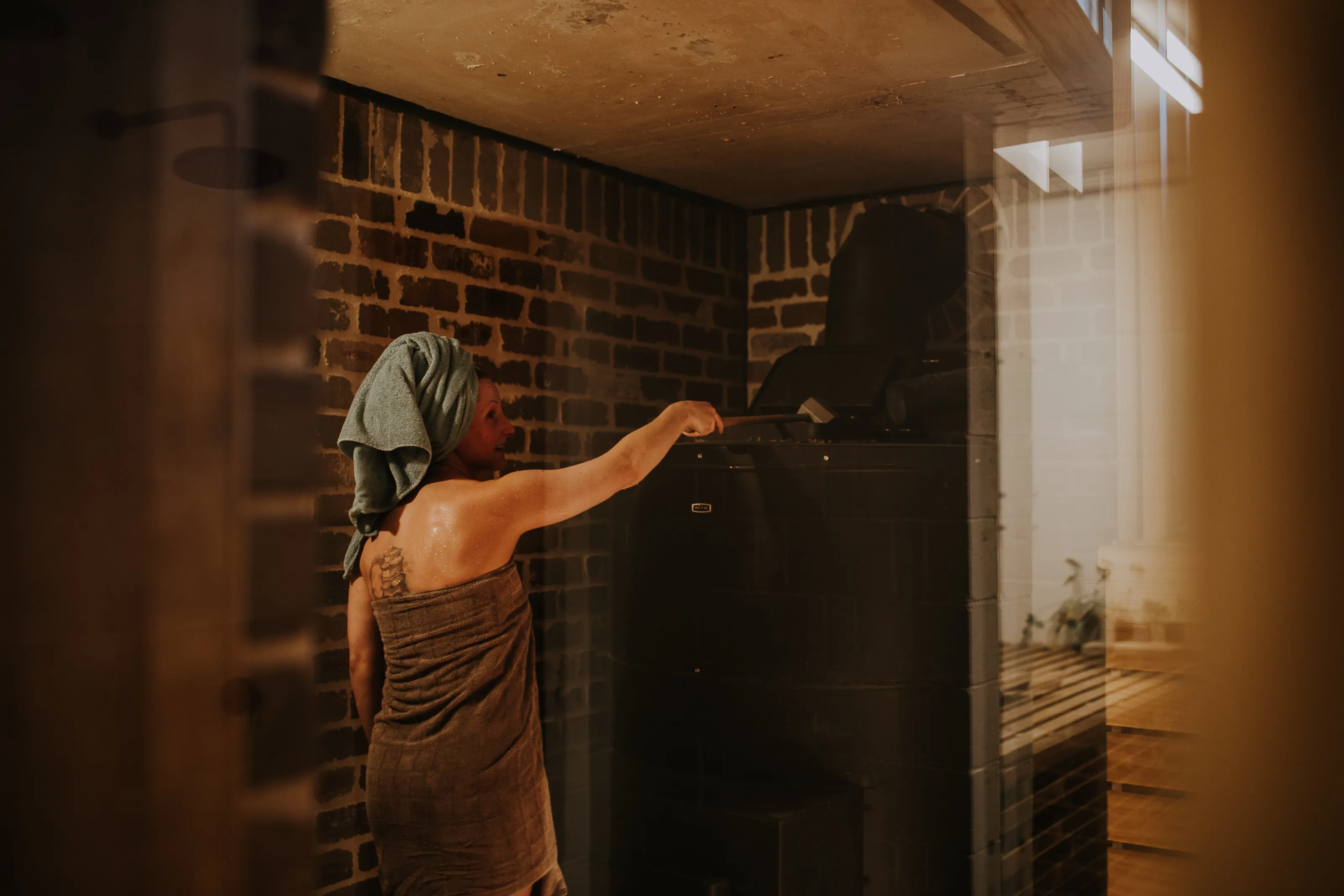 A bather ladles water onto the glowing stove at Blue Mountains Sauna as steam rises.