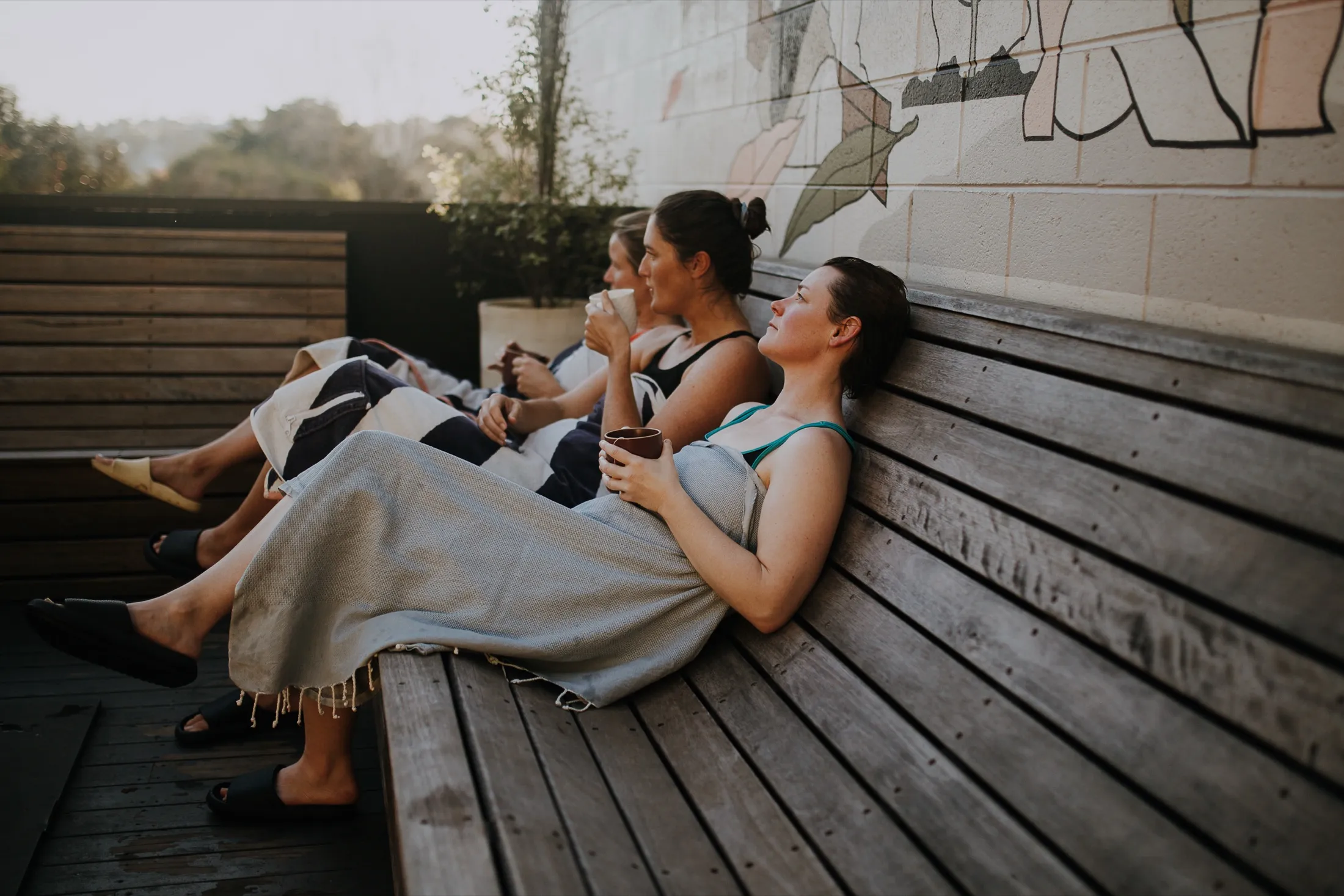 Guests wrapped in towels relaxing with tea on the timber bench