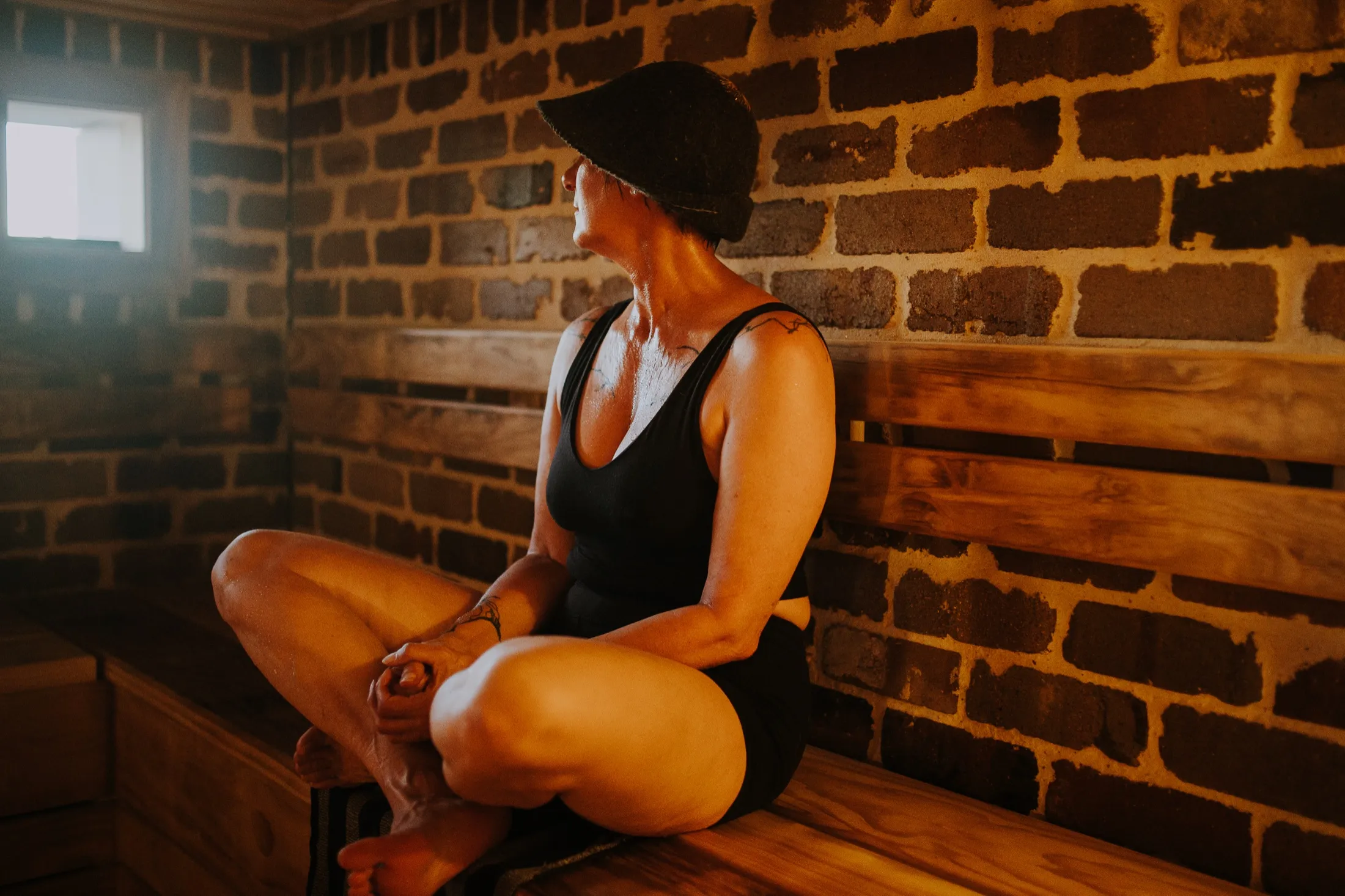 A bather in a felt sauna hat resting in the brick-walled Savusauna