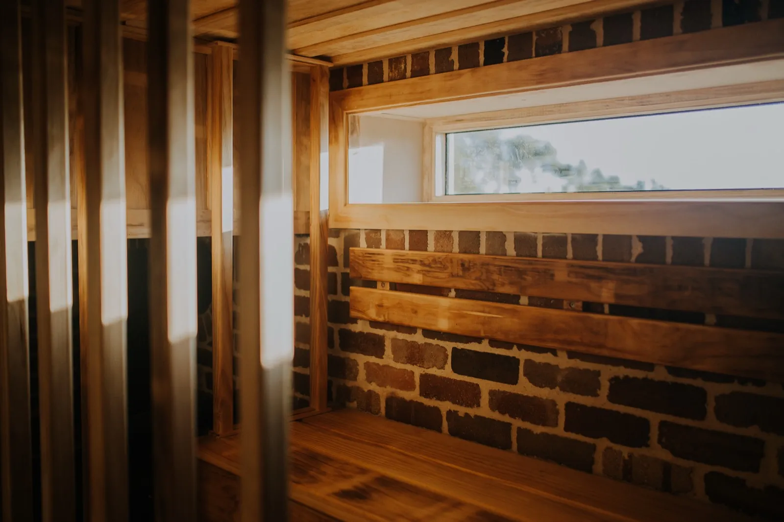 Inside the empty savusauna: timber benches, brick wall and window